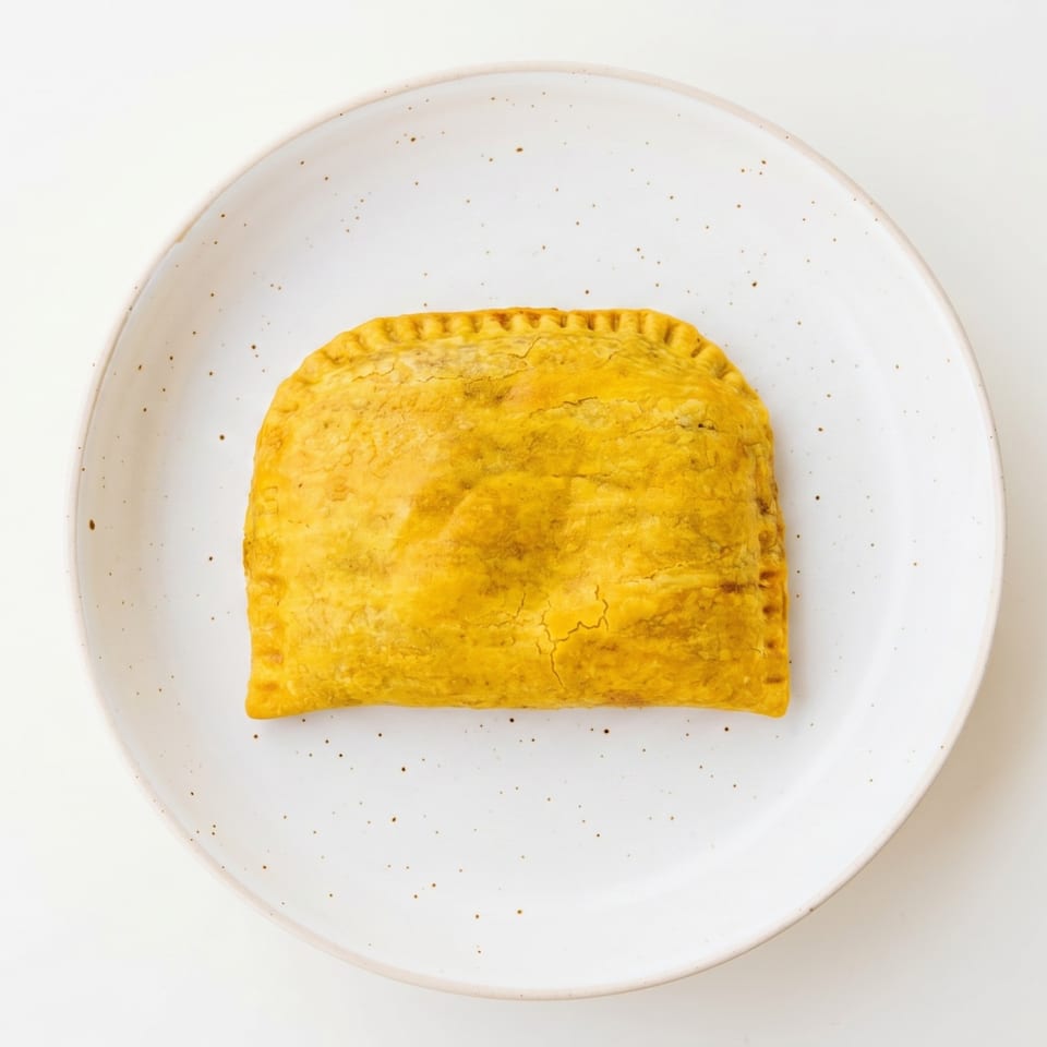 A golden-brown Jamaican beef patty with crimped edges rests on a speckled white plate.