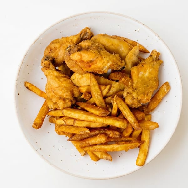 Crispy fried chicken wings and golden french fries served on a white speckled plate.