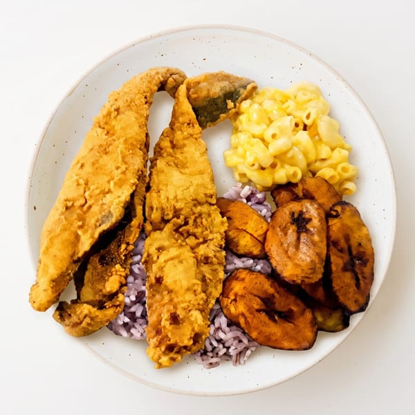 Fried fish, purple rice, mac and cheese, and plantains on a white plate.